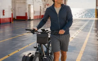 Mit dem Rad nach Dänemark: Mann mit Fahrrad an Bord einer Fähre, im Hintergrund das Meer